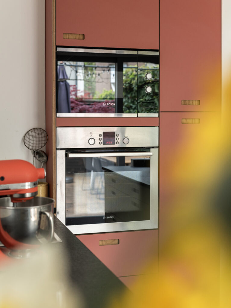 Électroménager moderne intégré dans des meubles de cuisine IKEA Faktum rénovés avec des façades terracotta et des poignées en bois.