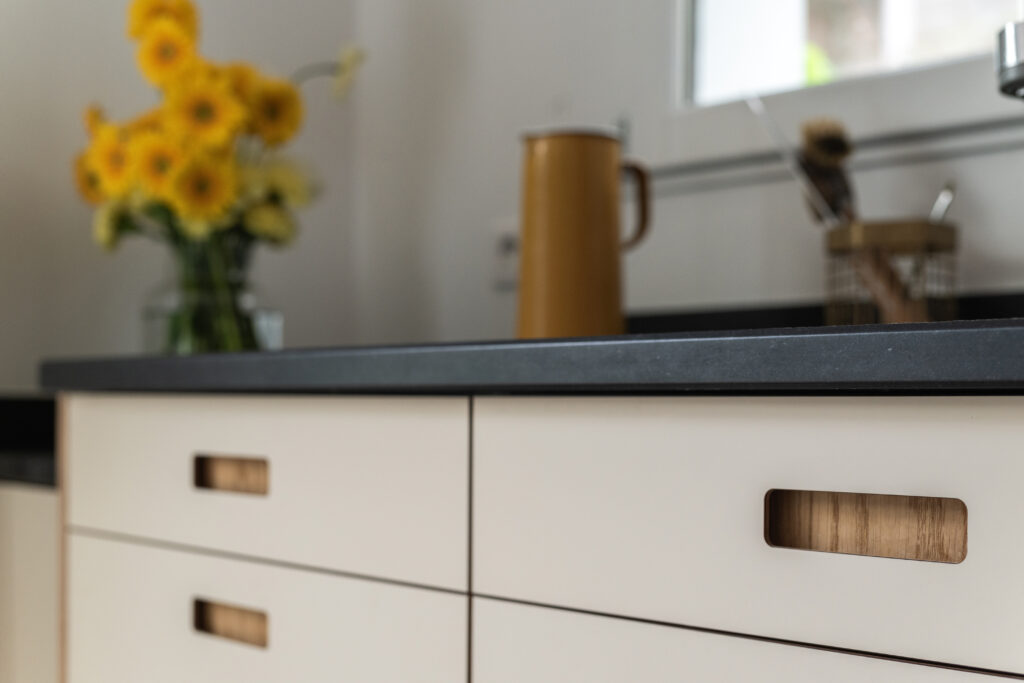 Cuisine IKEA Faktum avec plan de travail noir, fleurs jaunes en vase et façades beige avec poignées en bois.