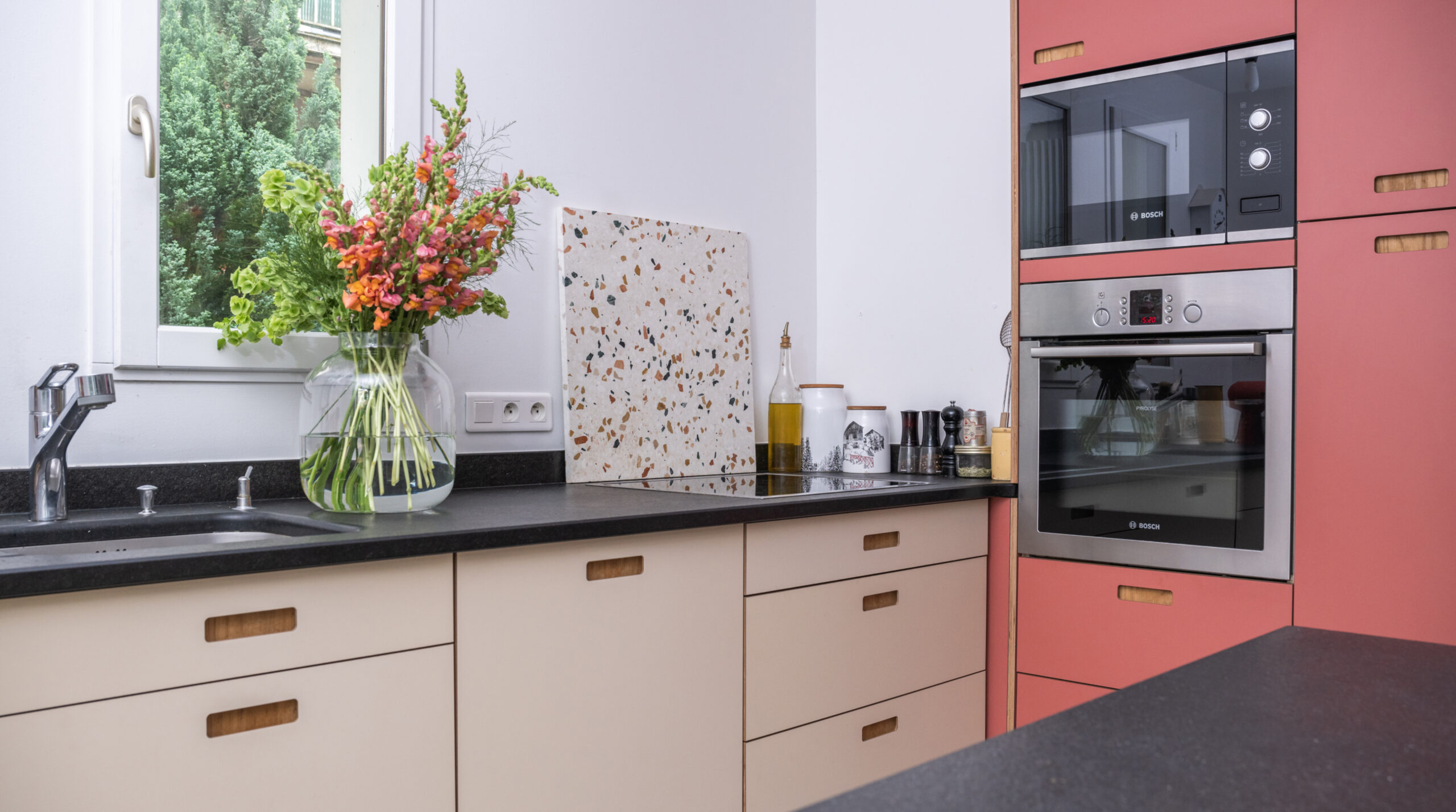 Vue d'ensemble d'une cuisine IKEA Faktum rénovée avec des façades Popline terracotta et beige, plan de travail noir, et une planche à découper terrazzo.