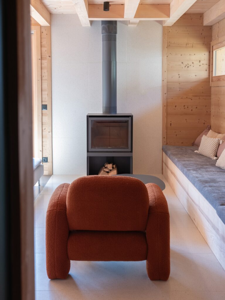 Fauteuil moderne en tissu dans un salon de chalet avec un poêle à bois.